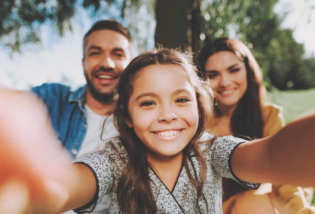 Een klein meisje die een selfie neemt samen met haar papa en mama in een park. 