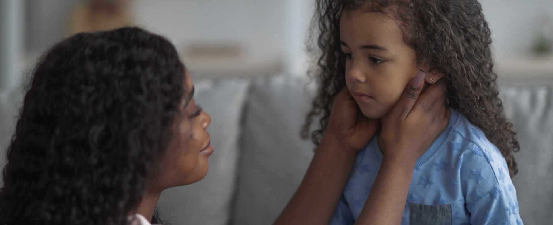 Een mama die haar handen op haar dochter haar kaken legt om haar te troosten. 