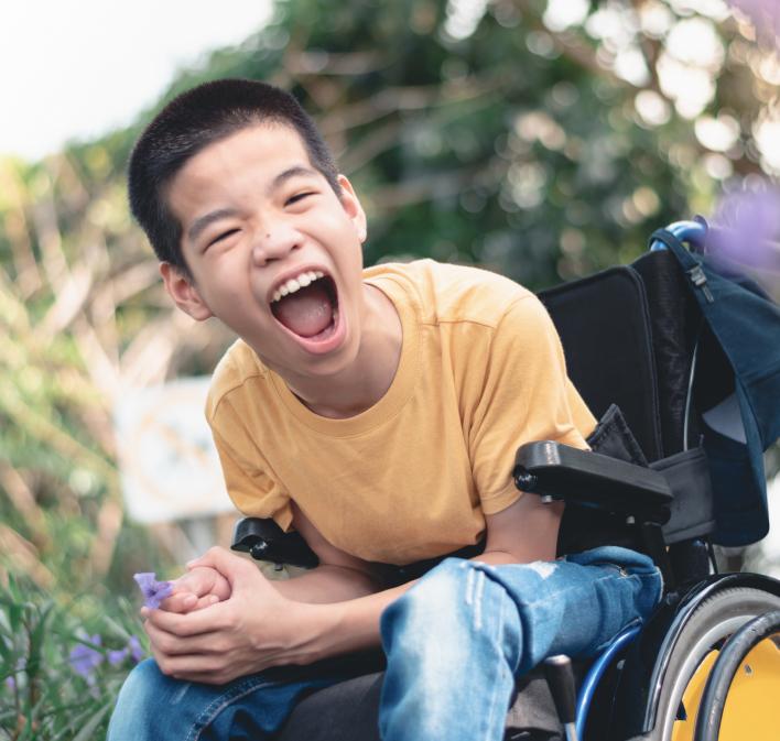 Een jongen die met een grote glimlach in een rolstoel zit terwijl hij een paarse bloem vastheeft.